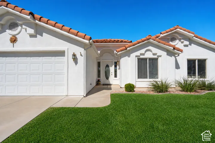 Stucco exterior with terracotta tile roofing, a concrete driveway, and a manicured lawnPhoto of lawn is altered to be more green.