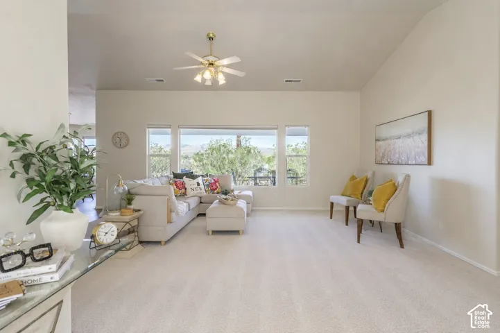 Bright, open living space featuring expansive windows with natural light, light wood-finish flooring throughout, ceiling fan with integrated lighting, and neutral wall finishes