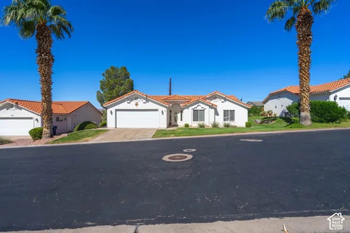 White stucco exterior with a terra cotta tile roof, attached two-car garage, and a manicured front lawn with mature landscaping