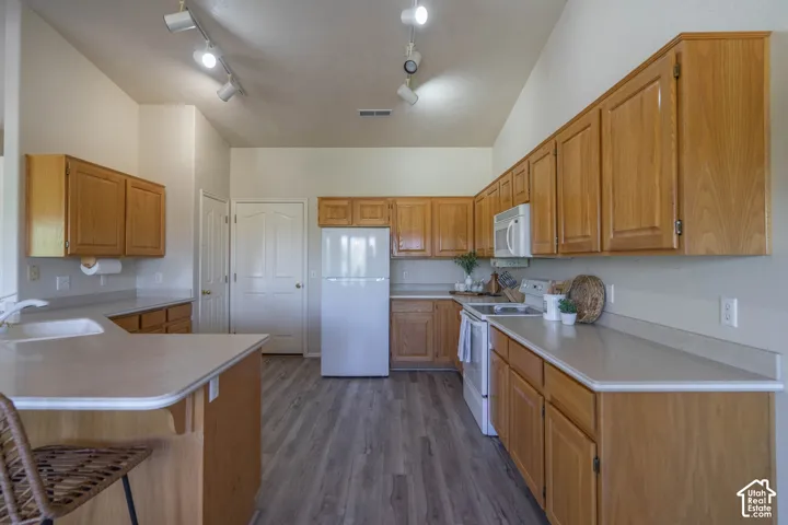 Vaulted ceiling kitchen featuring wood-finish cabinetry, light countertops, wood-finish flooring, and track lighting