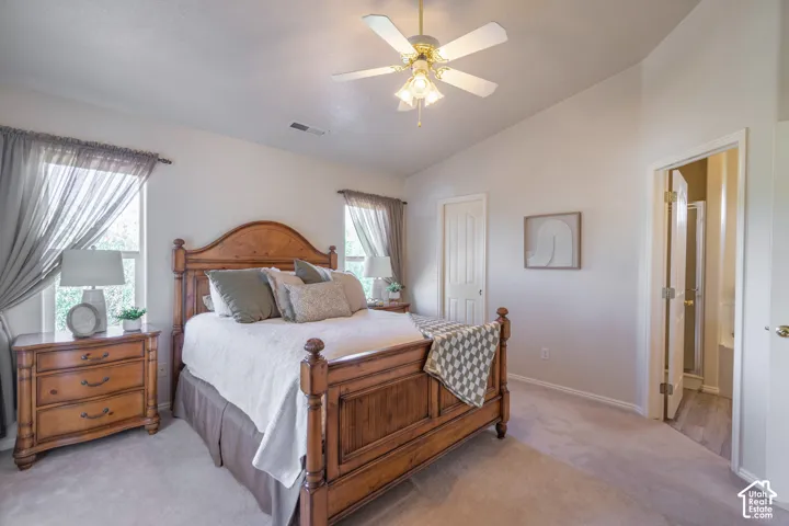 Vaulted ceiling with an attached ceiling fan, two windows with curtain rods, light-toned wall paint, and light-toned carpet flooring