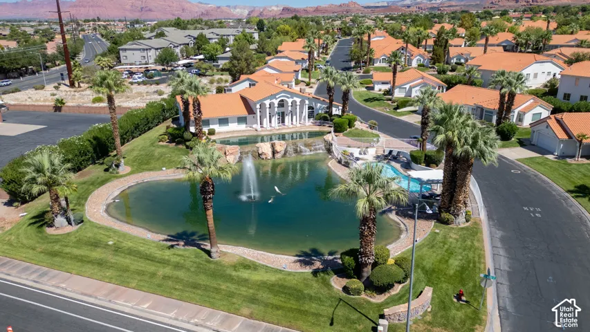 Community grounds featuring a central pond with a fountain, lush landscaping, mature palm trees, a swimming pool, and a clubhouse with classical architectural elements