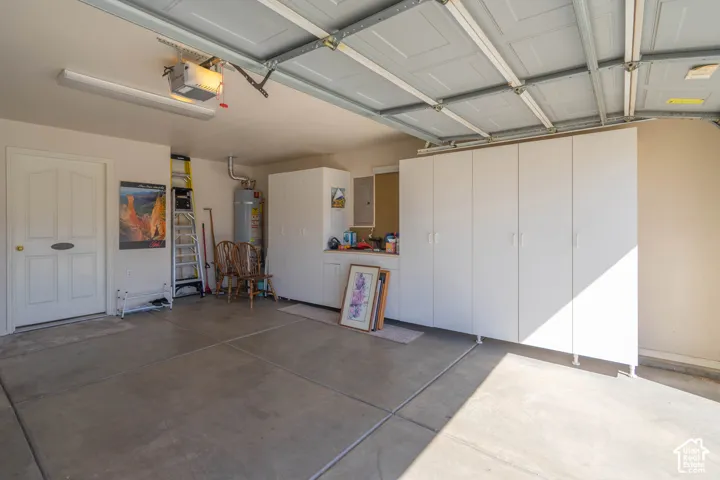 Concrete flooring, built-in white cabinetry, overhead fluorescent lighting, garage door opener, and a water heater