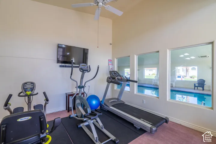 Recessed wall-mounted television, vaulted ceiling with a ceiling fan, and multiple windows overlooking a swimming pool