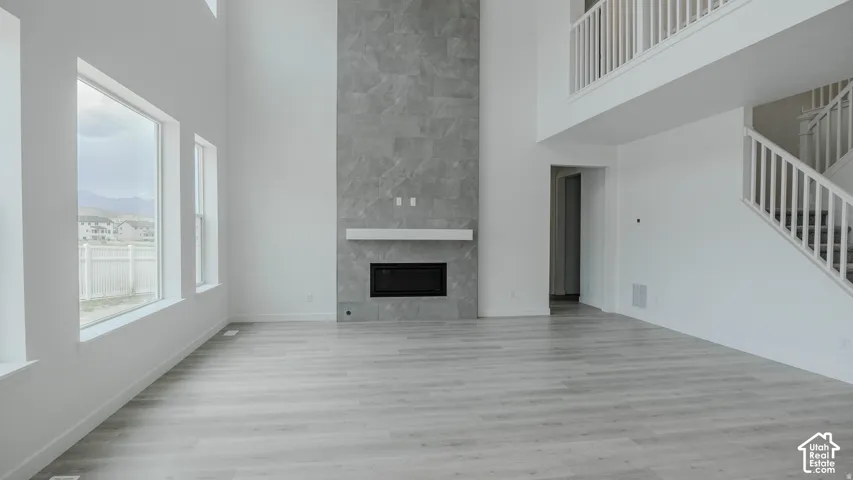 Two-story living area featuring a floor-to-ceiling tile fireplace with a white mantel, an integrated electric fireplace, multiple windows, and light wood-finish flooring