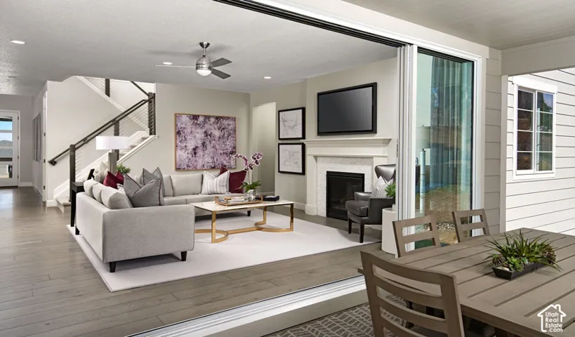 Wood-finish flooring, staircase with metal railings, built-in fireplace, ceiling fan, and sliding glass door