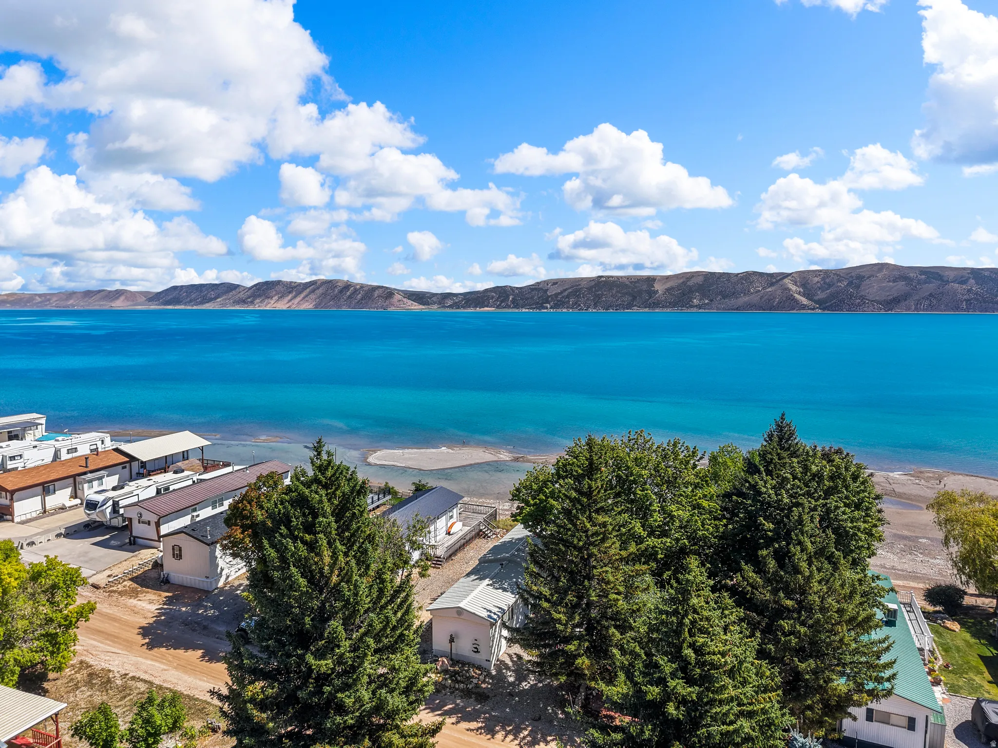 Expansive blue lakefront with a distant mountainous horizon, featuring several residential structures and mature trees along the shoreline
