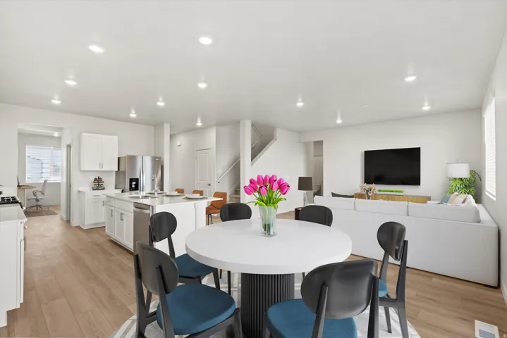 Open-concept living space featuring wood-finish flooring, recessed lighting, a white kitchen island with seating, stainless steel appliances, and white cabinetry