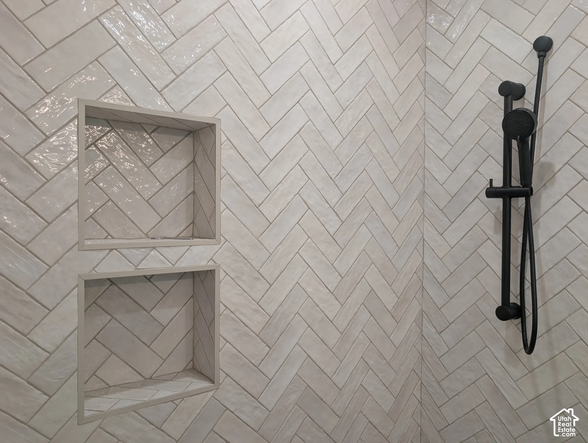 Herringbone tile shower wall with two recessed niches and a matte black shower system