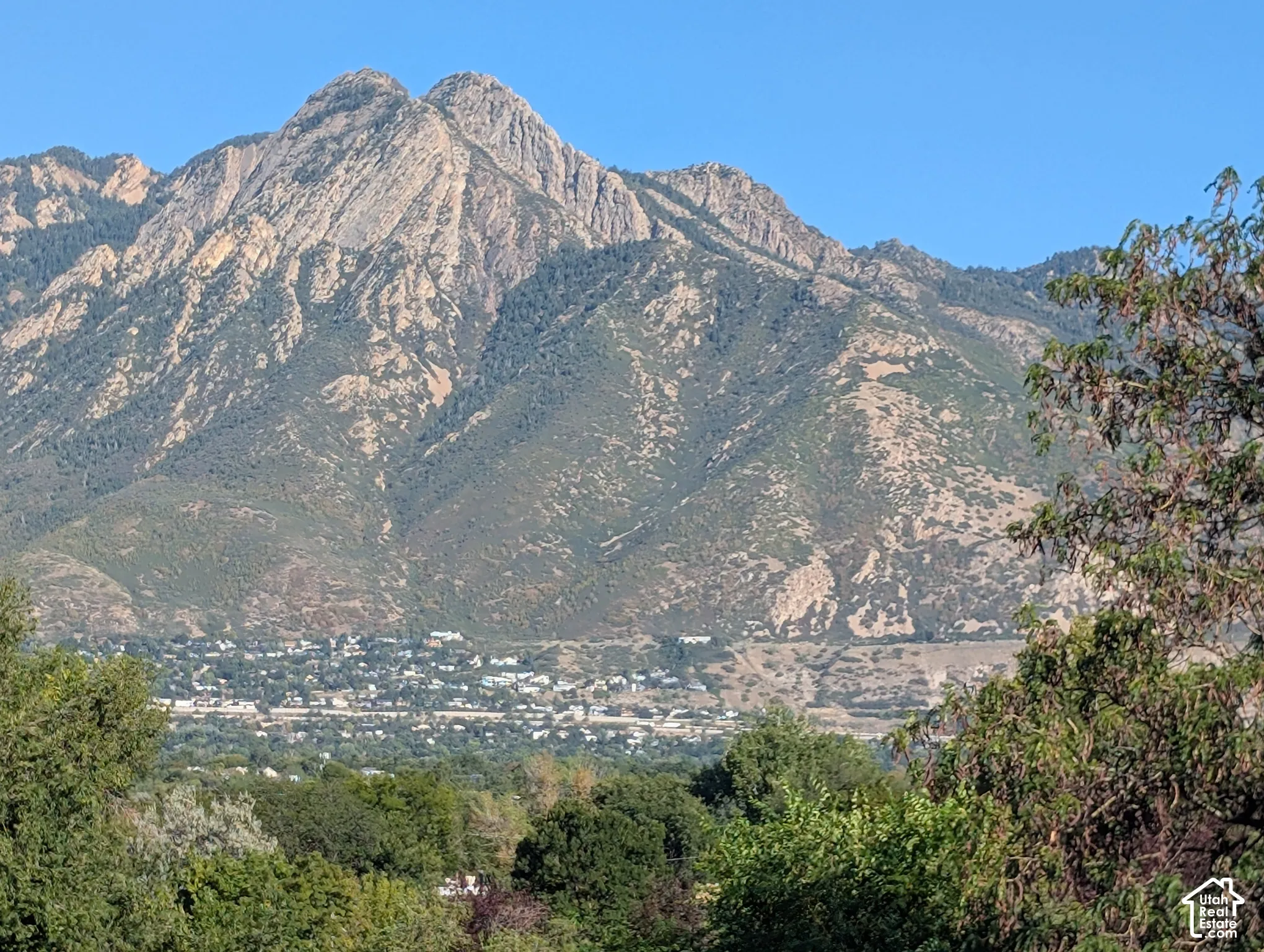 Mountain backdrop with natural rock formations, featuring a distant community with varied architecture, and foreground foliage