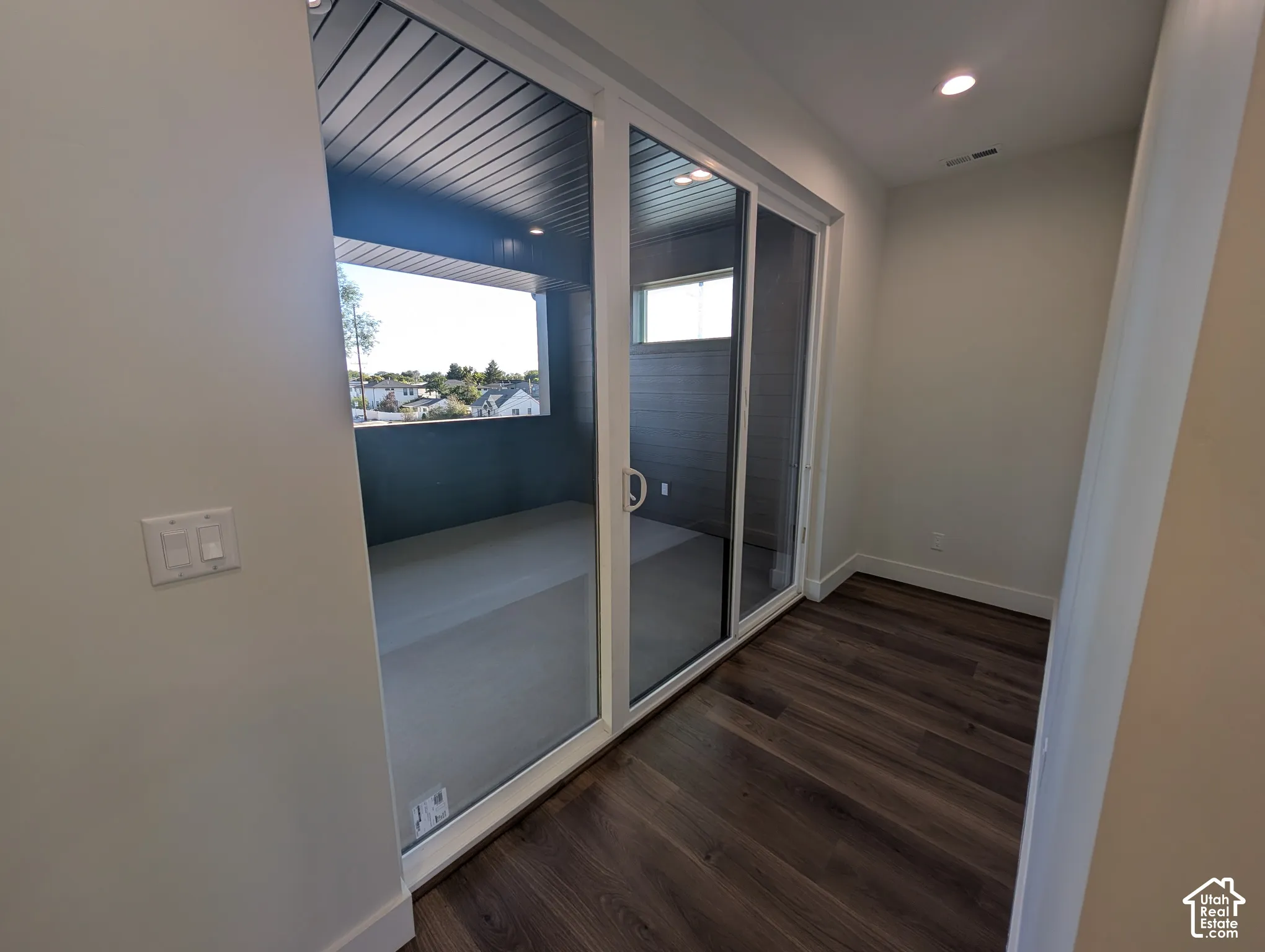 Sliding glass door leading to a covered balcony with dark wood-finish ceiling, featuring recessed lighting and dark wood-finish flooring