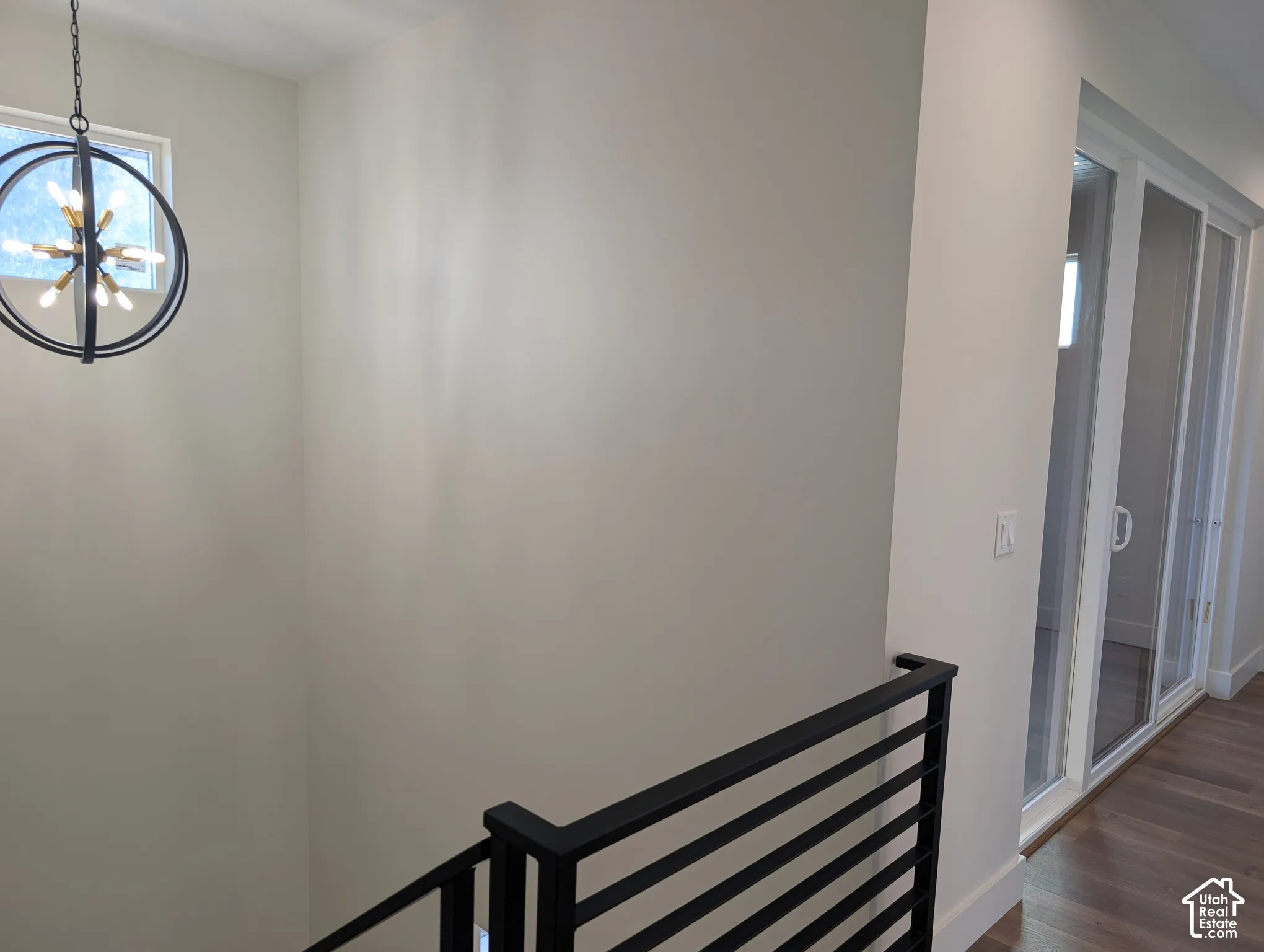 Modern spherical chandelier with exposed bulbs, black metal railing, light wood-finish flooring, and white-framed sliding glass doors