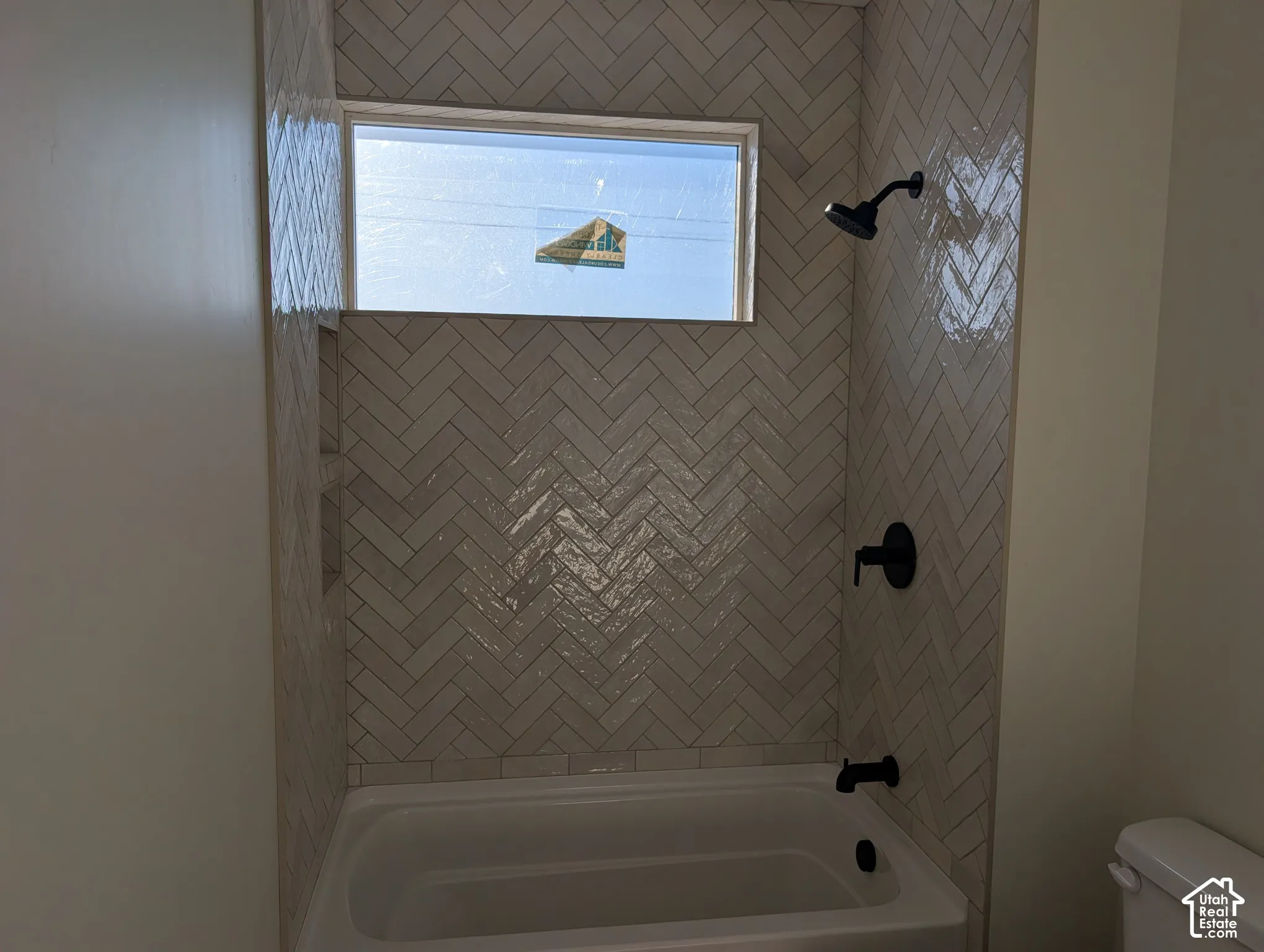 Bathtub with chevron-patterned tile surround, matte black shower fixtures, and an integrated window