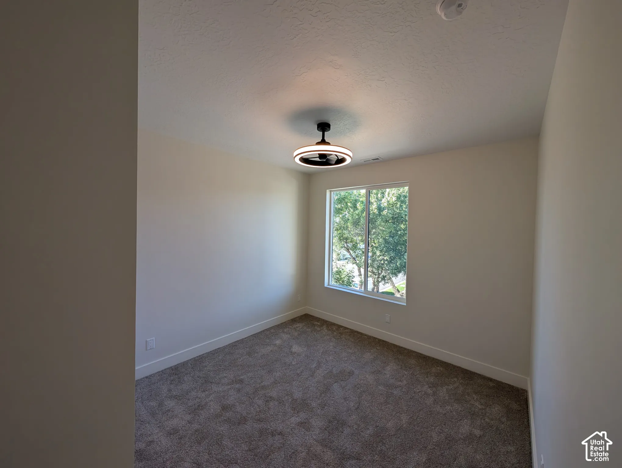 Neutral wall paint, textured ceiling, broad window, recessed lighting fixture, and carpeted flooring