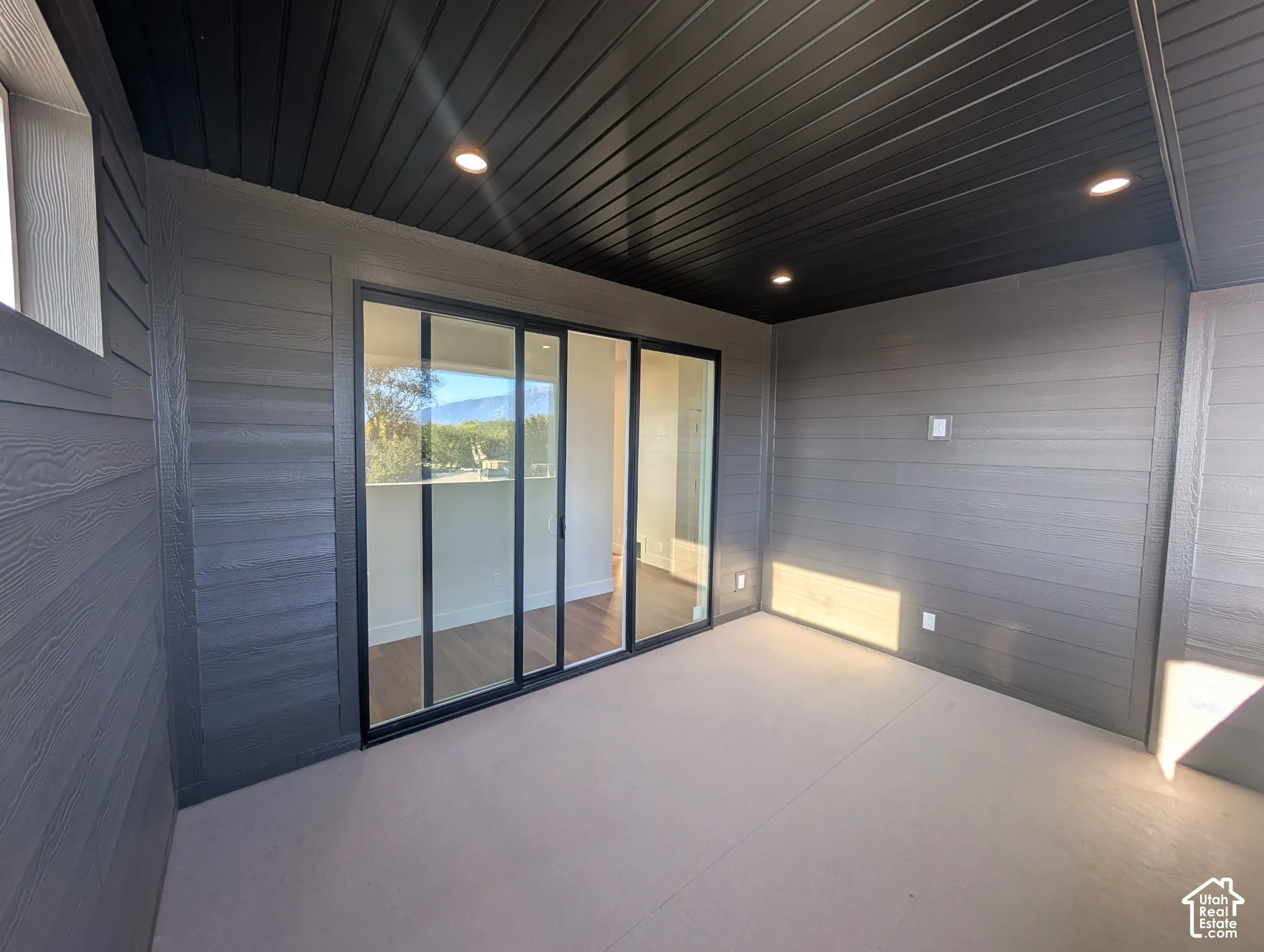 Covered outdoor patio with a black slatted ceiling, recessed lighting, and grey horizontal siding