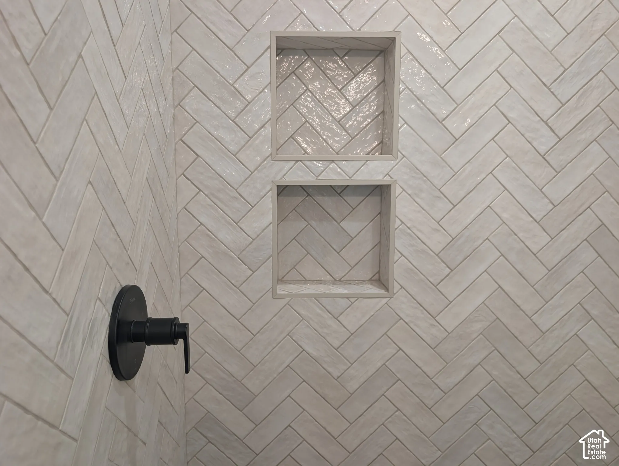 Herringbone pattern wall tile with two recessed shower niches and a matte black shower fixture