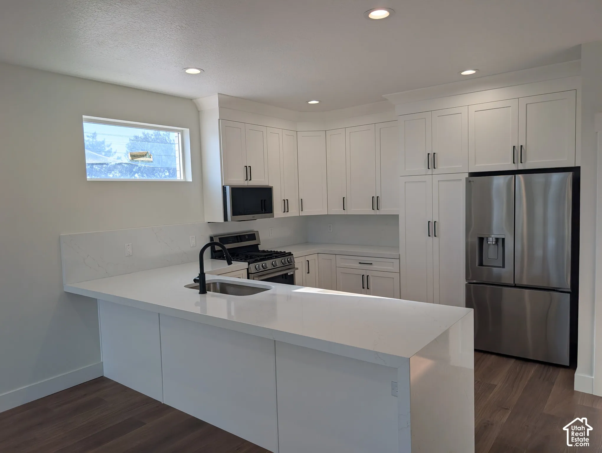 Kitchen featuring white cabinetry, stainless steel appliances, a black faucet, recessed lighting, and wood-finish flooring