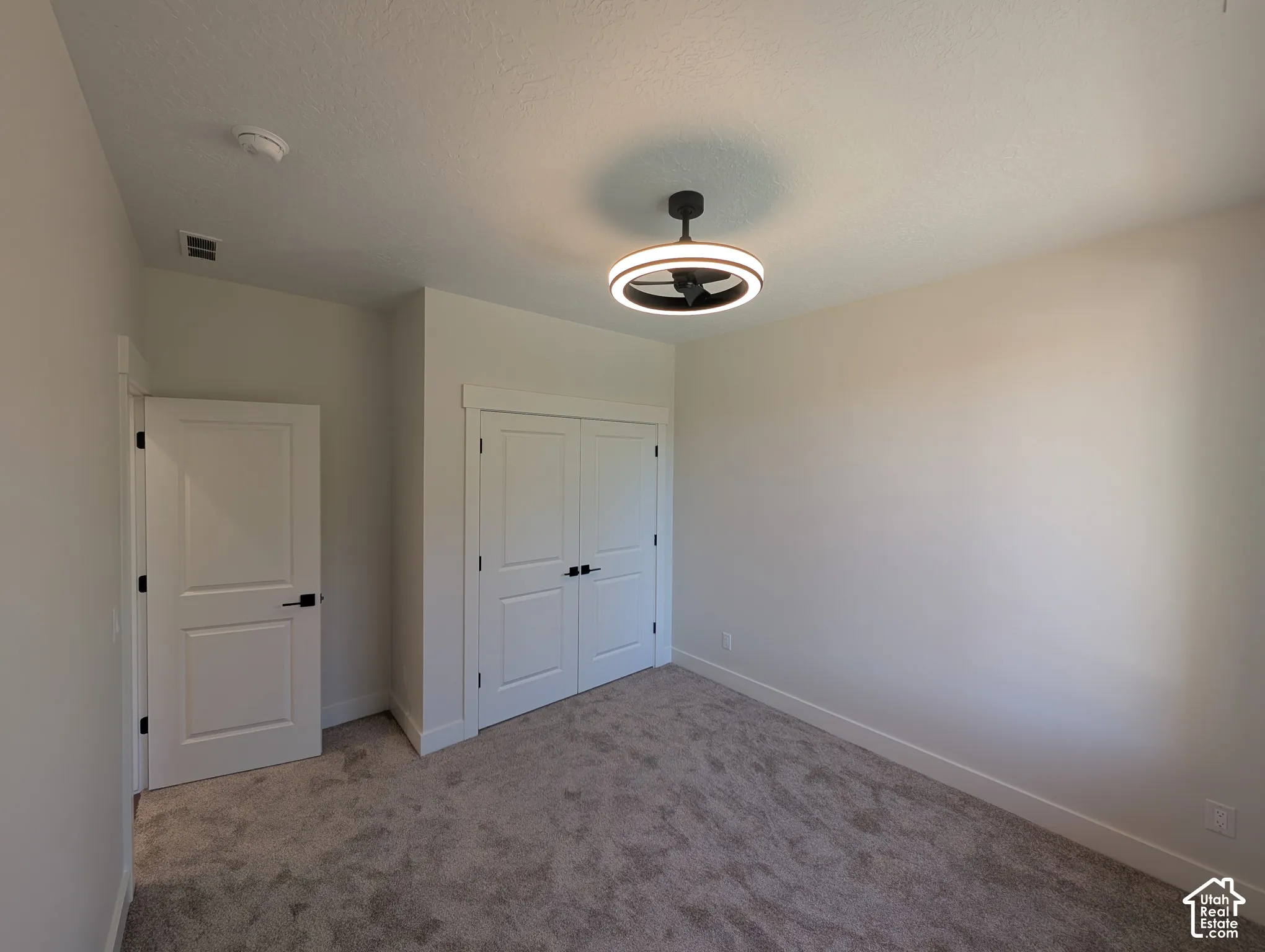 Ceiling-mounted fixture with integrated fan, double bifold closet doors, flat panel interior door, and textured carpeting