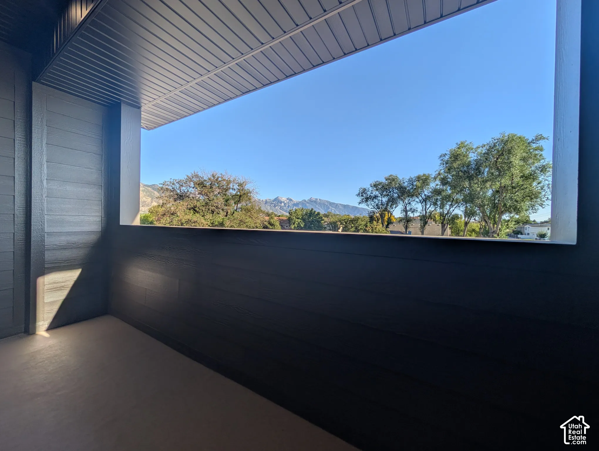 Covered outdoor balcony with mountain scenery, tree canopies, and a clear sky backdrop