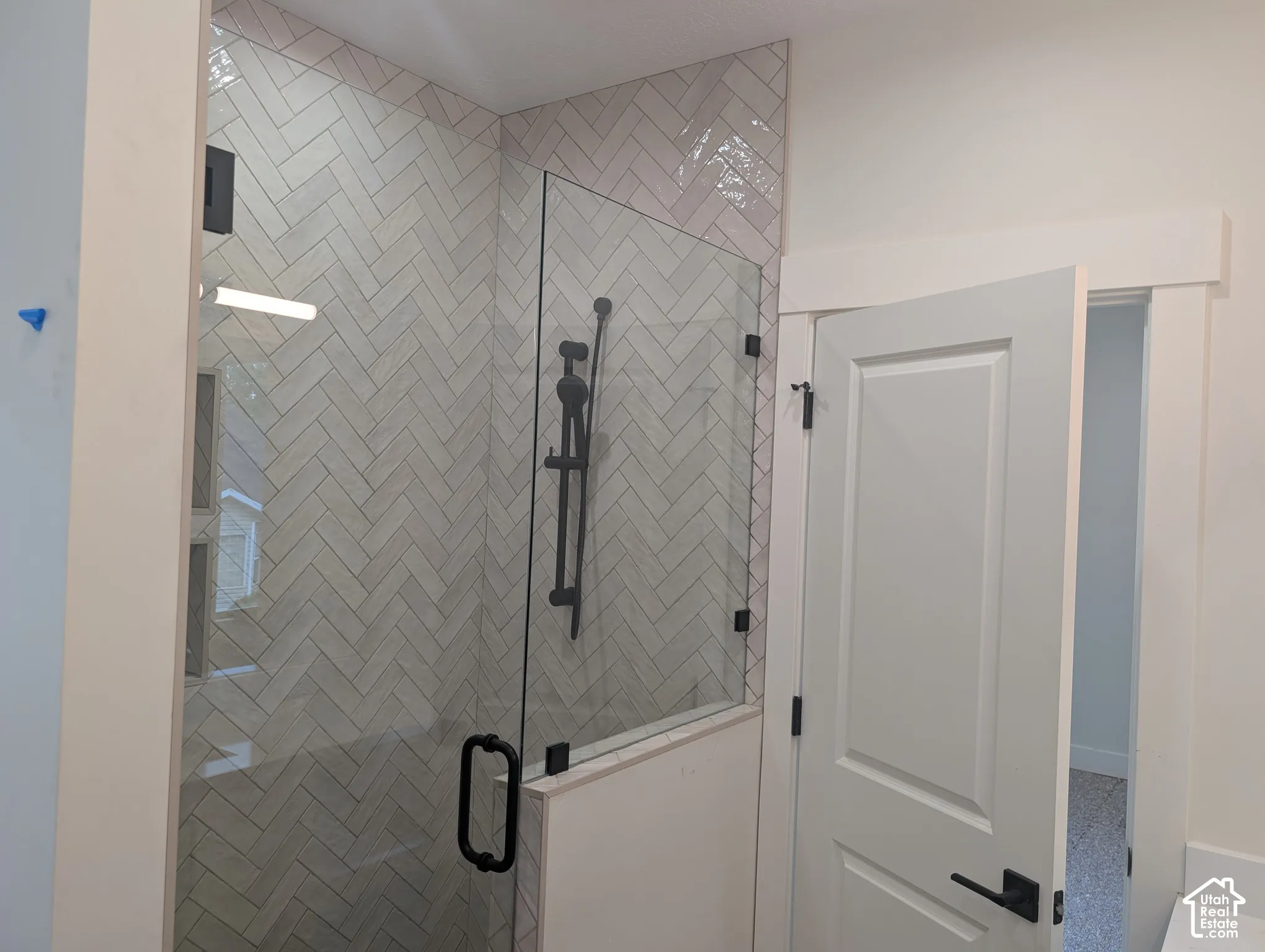Glass-enclosed shower with herringbone-patterned tile, matte black shower fixtures, and a coordinating matte black door handle