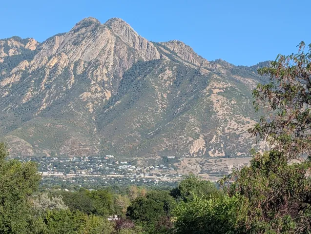Mountain backdrop with natural rock formations, featuring a distant community with varied architecture, and foreground foliage
