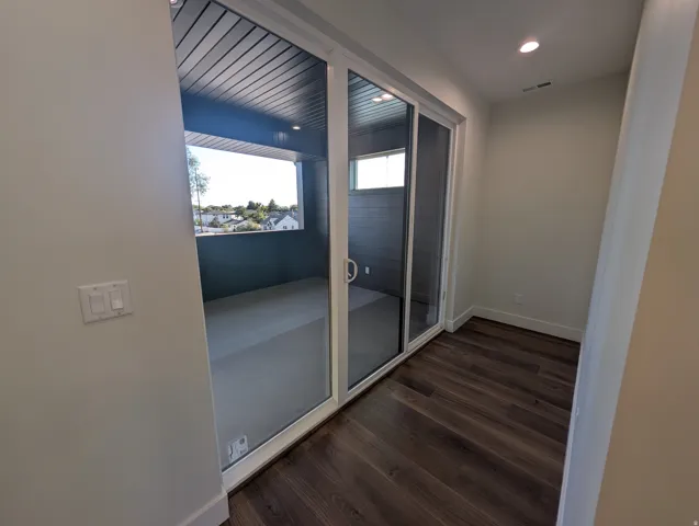 Sliding glass door leading to a covered balcony with dark wood-finish ceiling, featuring recessed lighting and dark wood-finish flooring