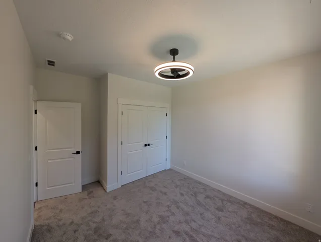 Ceiling-mounted fixture with integrated fan, double bifold closet doors, flat panel interior door, and textured carpeting