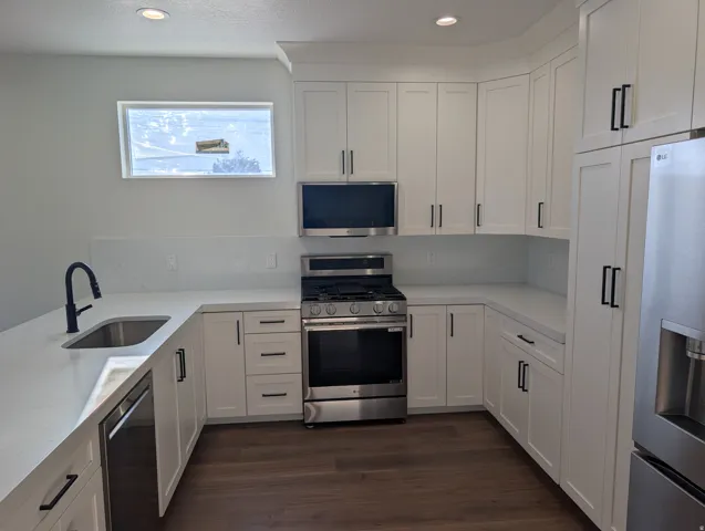 Kitchen featuring white shaker cabinetry, stainless steel appliances, a matte black faucet, white countertops, and wood-finish flooring