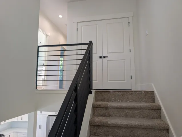 Carpeted staircase featuring a contemporary black metal railing and white paneled doors