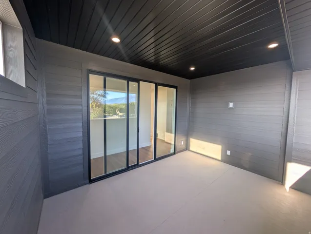 Covered outdoor patio with a black slatted ceiling, recessed lighting, and grey horizontal siding