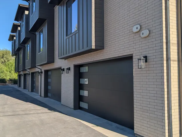Contemporary exterior with light brick and dark vertical siding, featuring modern garage doors with frosted glass panels, and black exterior lighting fixtures