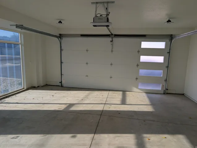 Spacious garage featuring a modern overhead door with frosted glass panels, an automatic opener, and polished concrete flooring