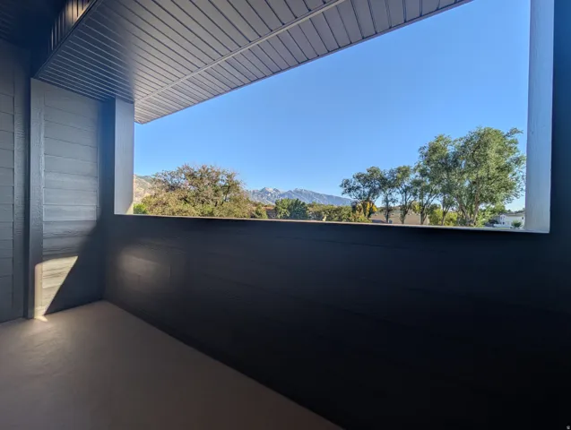 Covered outdoor balcony with mountain scenery, tree canopies, and a clear sky backdrop