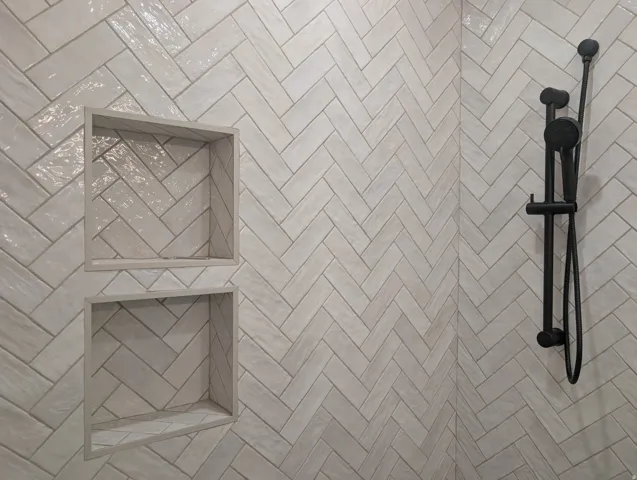 Herringbone tile shower wall with two recessed niches and a matte black shower system