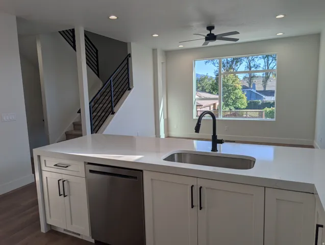 Kitchen island with white shaker cabinetry, stainless steel dishwasher, and an undermount sink with a matte black faucet