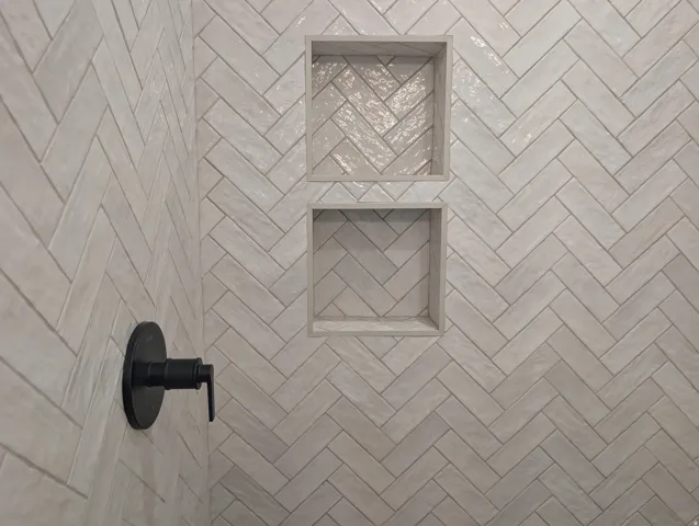 Herringbone pattern wall tile with two recessed shower niches and a matte black shower fixture