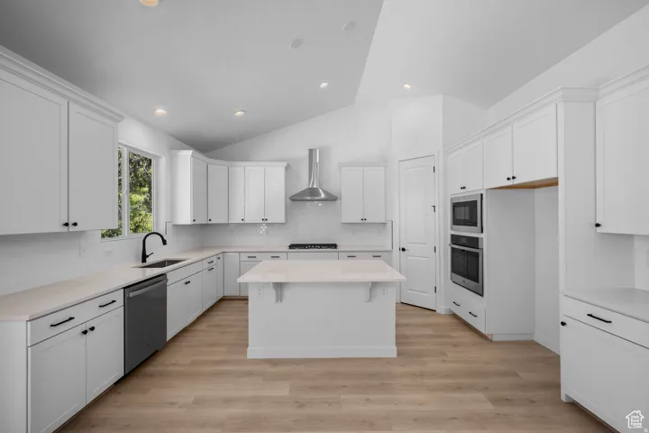 Modern kitchen featuring wood-finish flooring, white cabinetry, integrated stainless steel appliances, a center island, and vaulted ceilings