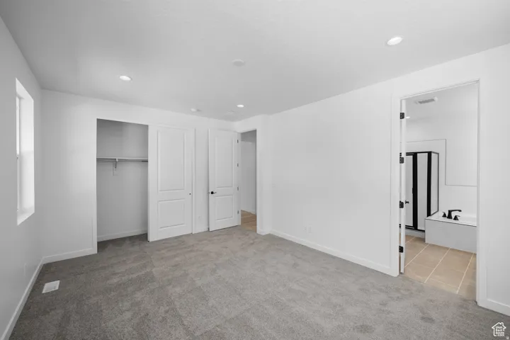 Plush grey carpeting, bright white walls, recessed ceiling lighting, sliding closet doors, and interior access to a bathroom