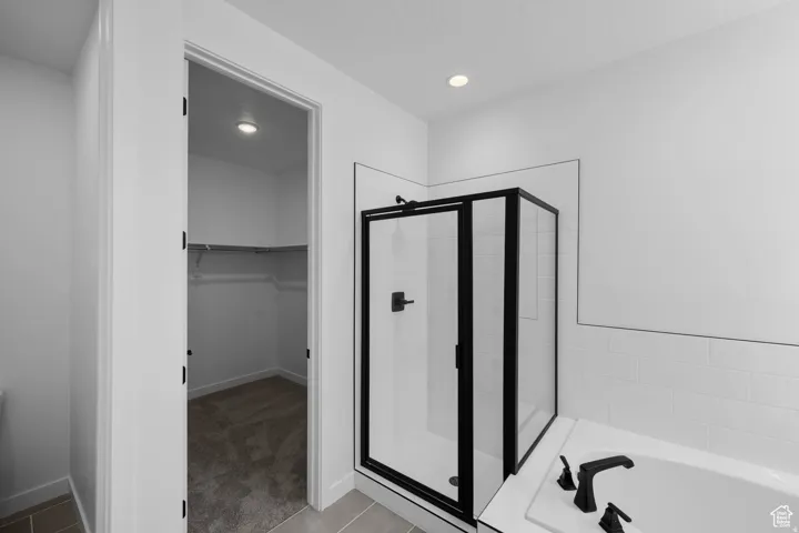 Walk-in closet with integrated shelving, corner shower with dark-framed glass enclosure, white subway tile surround, recessed lighting, and a built-in bathtub with dark fixtures