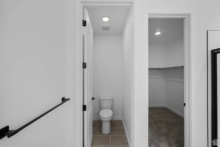 White walls with recessed lighting, a toilet in an alcove with tile flooring, and an open closet featuring carpet flooring and built-in shelving