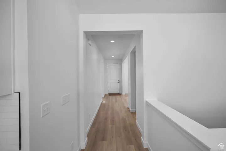 Hallway featuring wood-finish flooring, recessed lighting, and crisp white walls