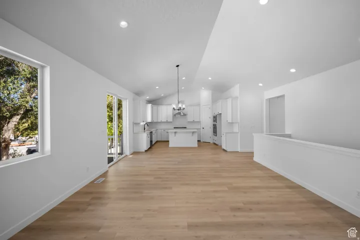 Vaulted ceilings, recessed lighting, wood-finish flooring, white kitchen cabinetry, and a sliding glass door