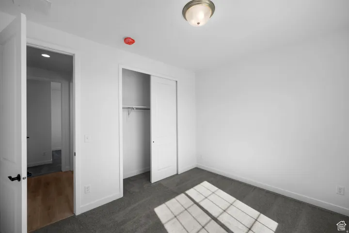Carpeted flooring, white walls, built-in closet with sliding doors, flush mount ceiling light, and an interior door with black hardware
