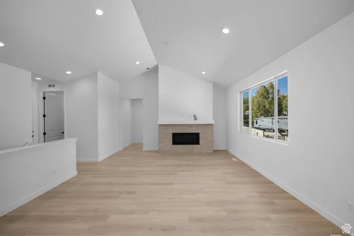 Vaulted ceilings, recessed lighting, wood-finish flooring, a contemporary fireplace with stone surround, and a large window