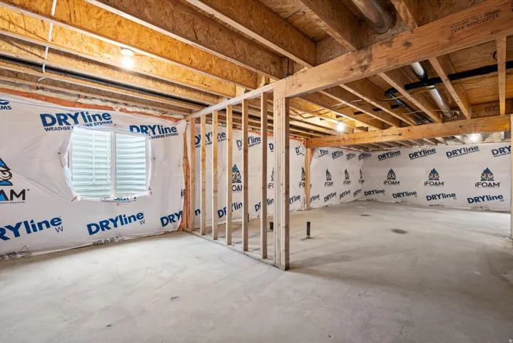 Unfinished basement featuring exposed wood joists, concrete flooring, perimeter wall insulation, and a visible egress window