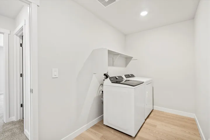Laundry area featuring wood-finish flooring, white walls, and a built-in shelf
