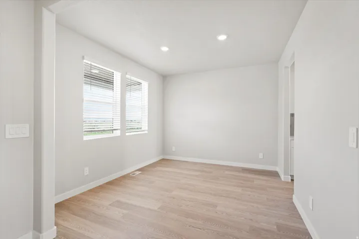 Recessed ceiling lighting, two windows with blinds, light wood-finish flooring, and white trim