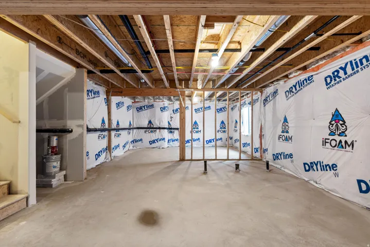Unfinished basement with concrete flooring, exposed wood joists, and framed walls featuring weather barrier insulation
