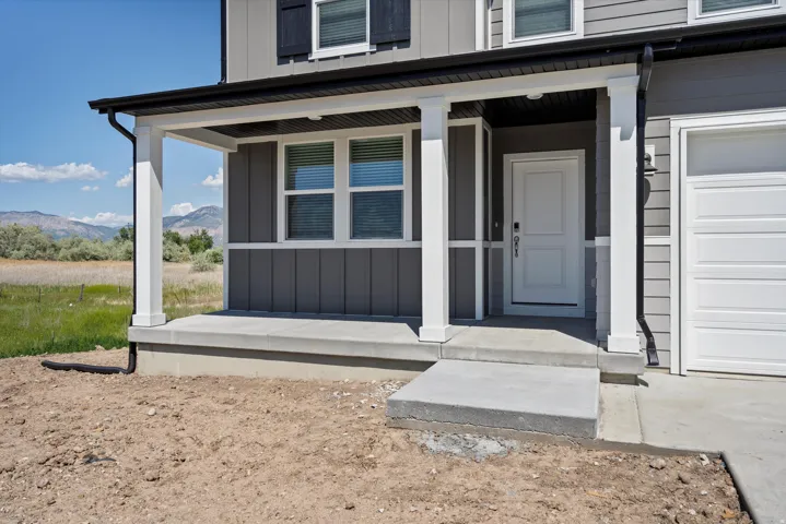 Covered front porch with white columns, concrete steps, and a white entry door