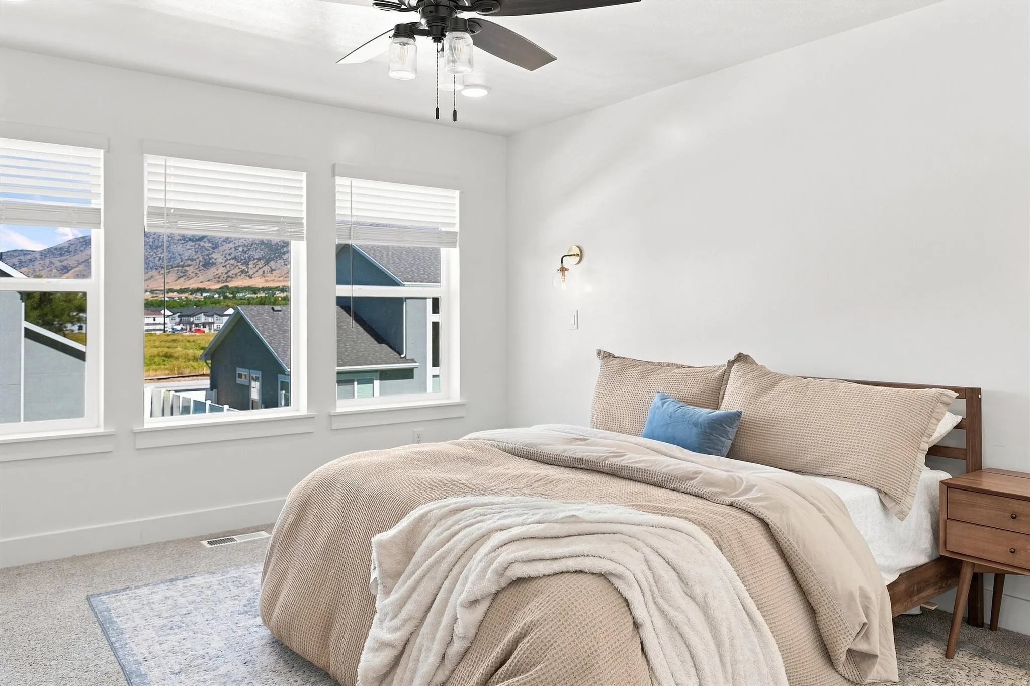 Triple windows with blinds, wall-mounted sconce, ceiling fan with integrated lighting, and carpeted flooring
